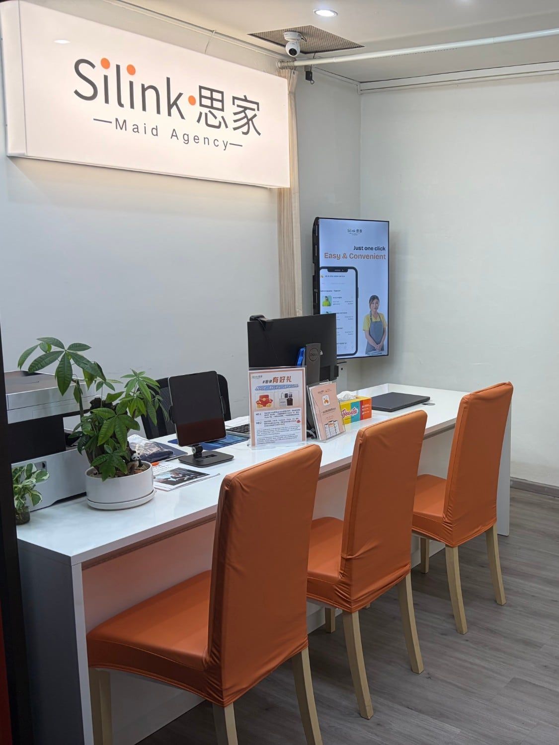 Inside the shop: the Silink sign and a wall screen showing the app above a long white desk with orange chairs.